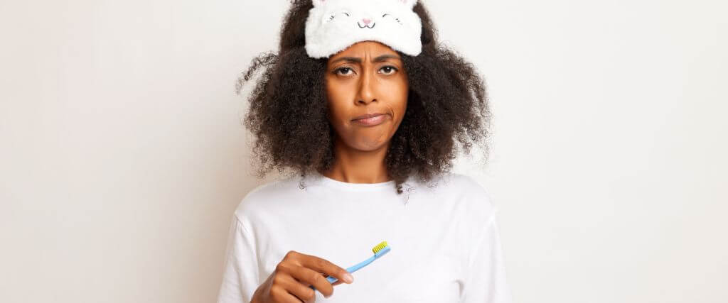 Woman tired from sleep brushing her teeth.